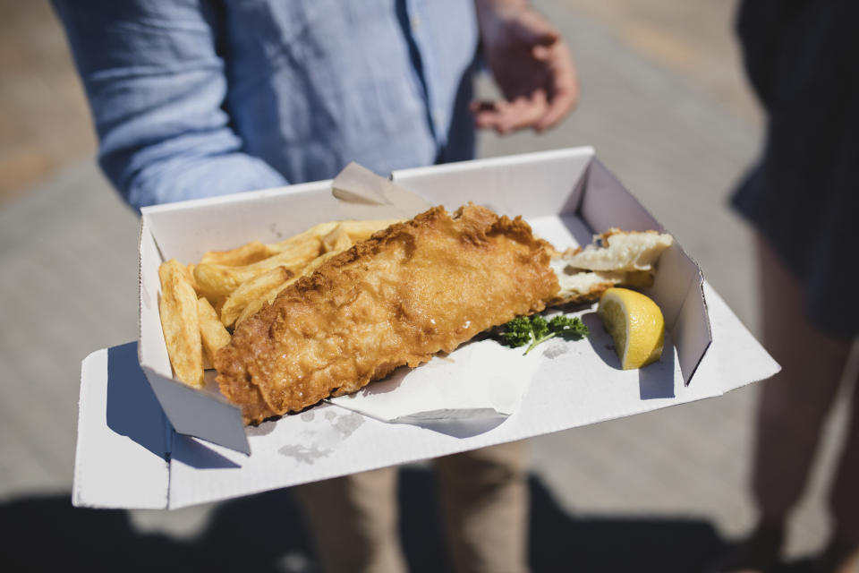 Person holding a box of battered fish and chips, typically British food, British food, takeaway